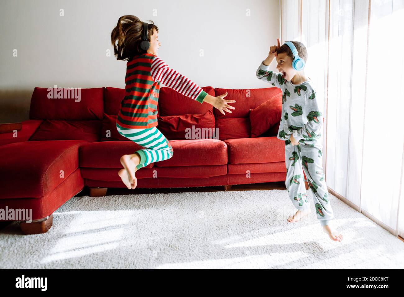 Male and female sibling wearing headphones while dancing against sofa in living room Stock Photo