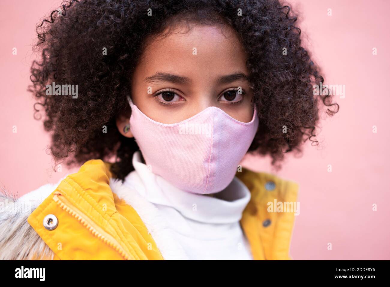 Girl wearing pink face mask standing against pink wall Stock Photo