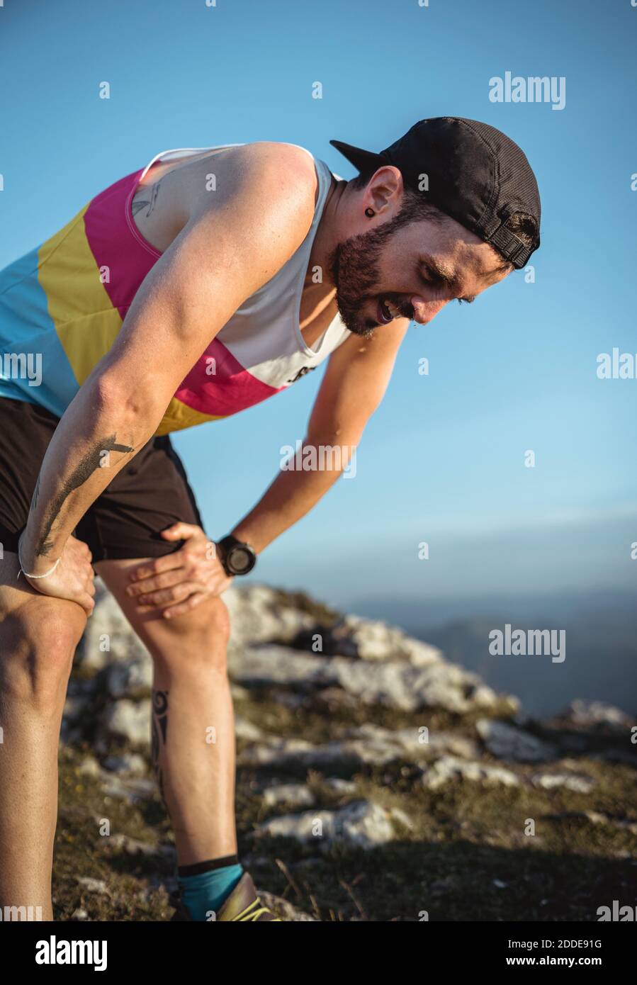 Tired man with hand on knee standing on mountain against clear sky Stock Photo