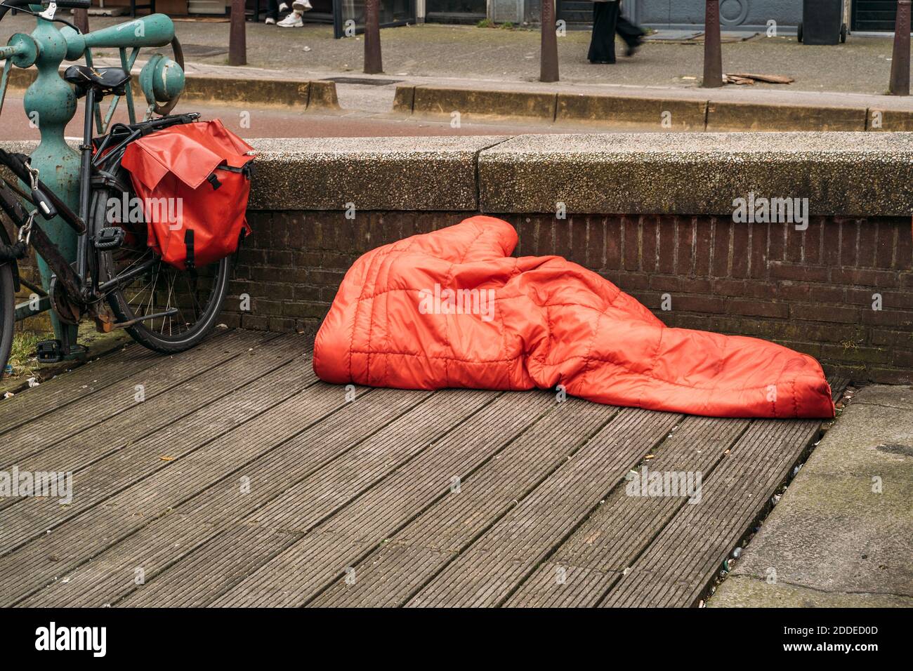 Homeless man sleeps under red blanket in center of European city. Stock Photo