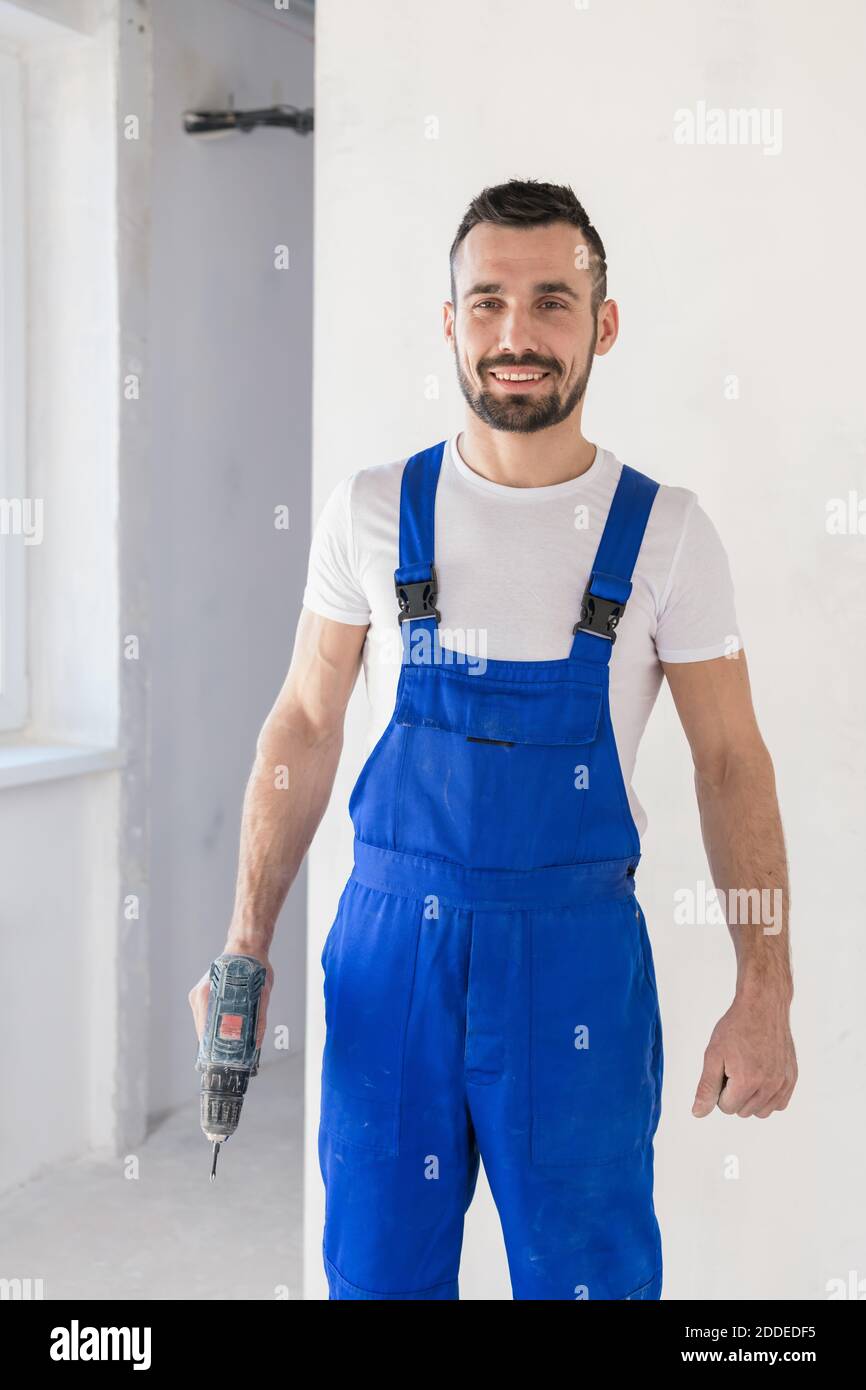 Repairer in blue overalls posing with a drill Stock Photo Alamy
