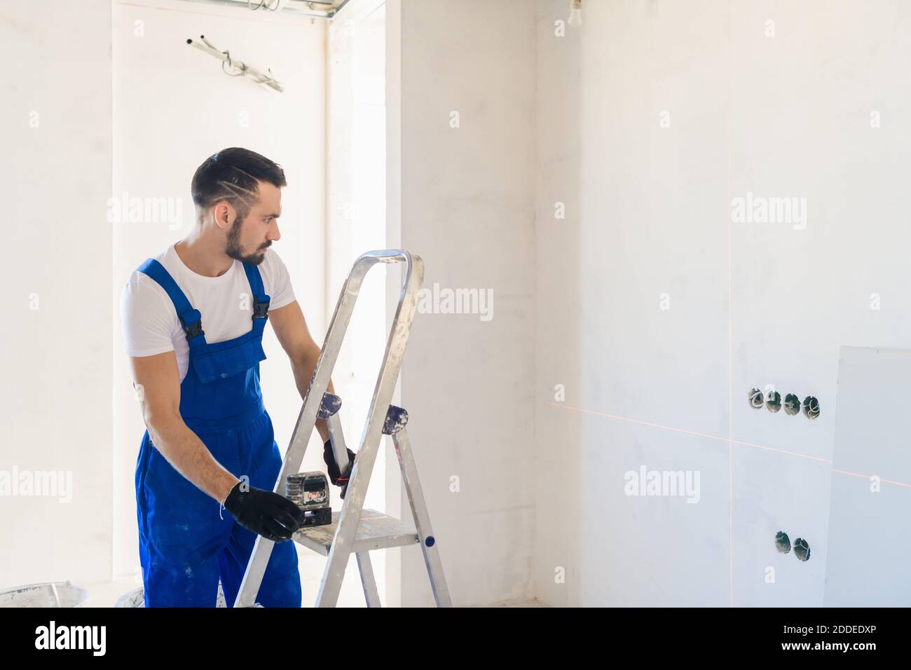 A handyman in overalls marks the wall using a laser level Stock Photo