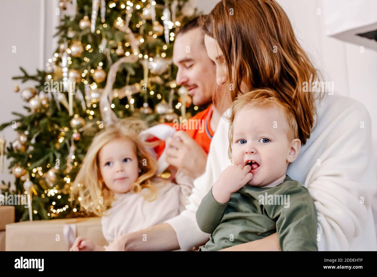 Portrait of friendly family are sitting at home near the Christmas tree, everyone is smiling. Focus on baby. Stock Photo