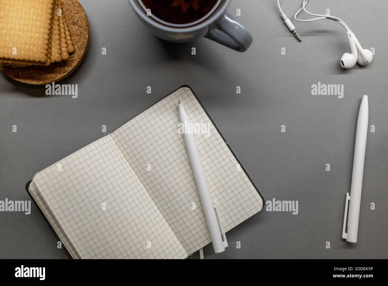 open notebook cup cookie and pens on grey table Stock Photo