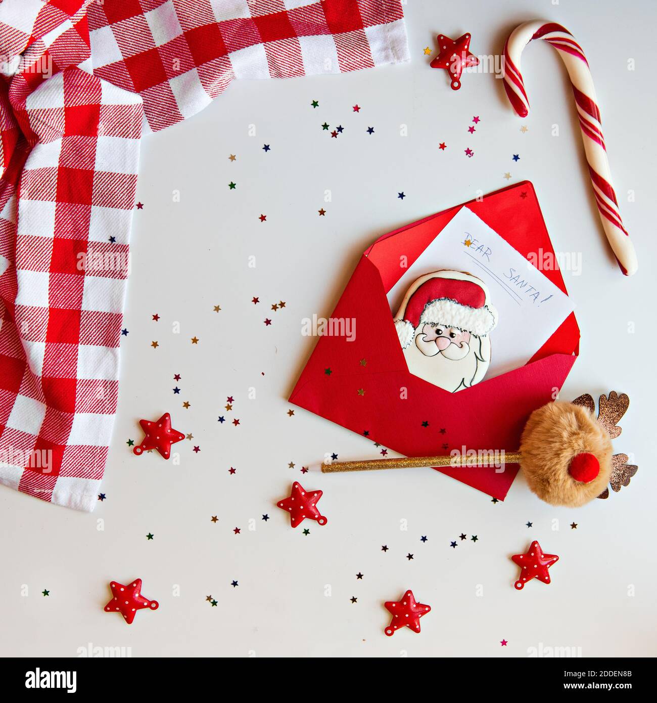 Flatlay New Year's in white and red colors. Christmas card with stars confetti. A letter to Santa Claus with a gingerbread cookie. Deer pom-pom handle Stock Photo