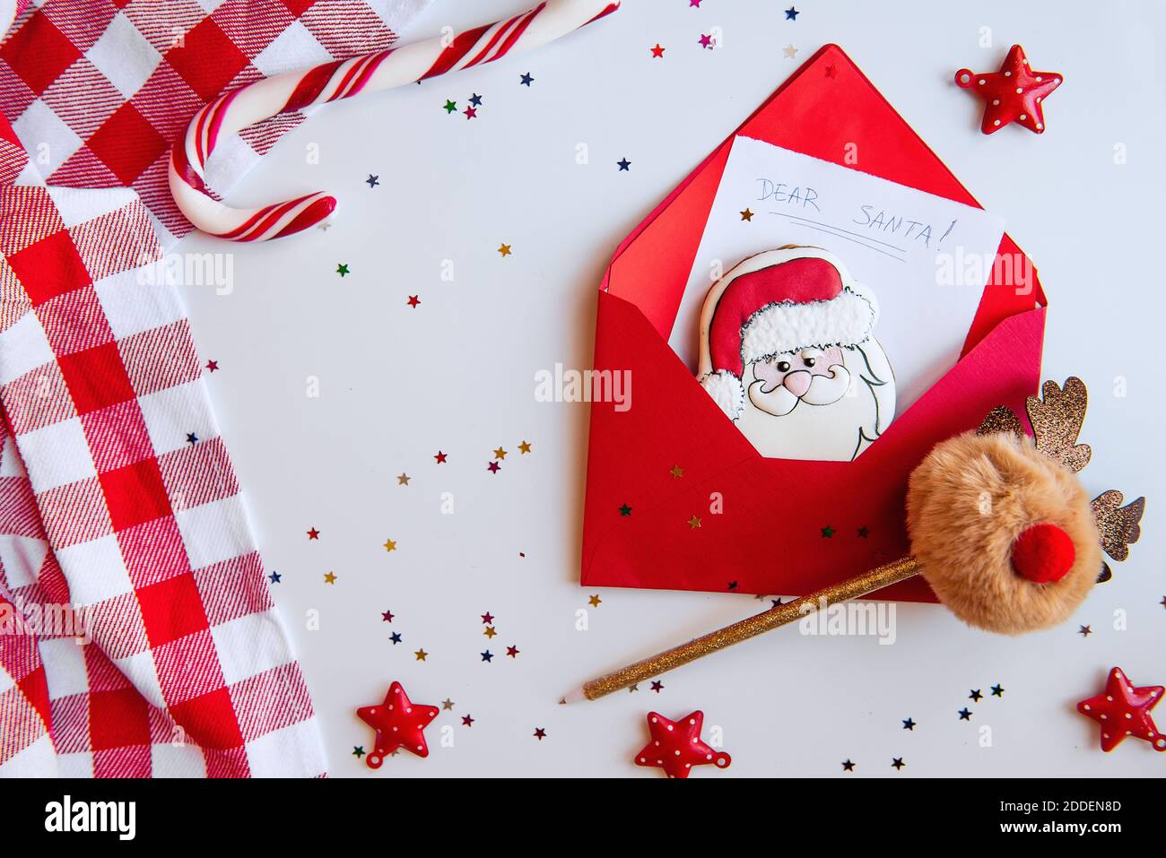 Flatlay New Year's in white and red colors. Christmas card with stars confetti. A letter to Santa Claus with a gingerbread cookie. Deer pom-pom handle Stock Photo