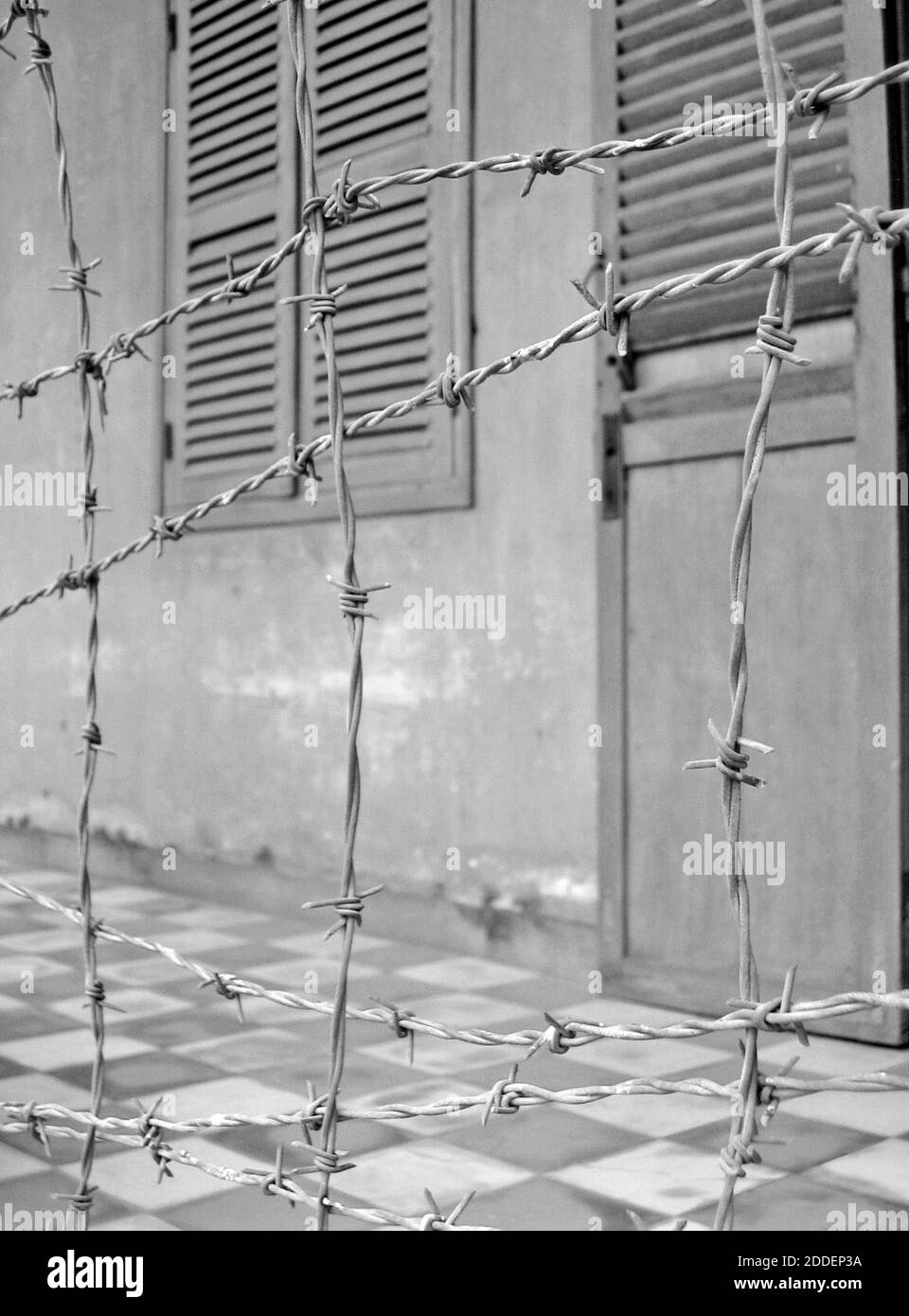 Barbed wire acts as one of barriers used by the Khmer Rouge in what is now the Tuol Sleng Genocide Museum in Phnom Penh, Cambodia.  Once a secondary school, Tuol Sway Pray High School, from 1976-1979 it became Security Prison 21 (S-21).  Composed of several buildings, the campus became an internment camp where an estimated 20,000 persons were imprisoned, tortured, and died.  Enclosed in electrified barbed wire, the former school was uncovered by the conquering Vietnamese Army.  Out of the over 20,000 prisoners, there were 12 known survivors.  The school is now the Tuol Sleng Genocide Museum. Stock Photo