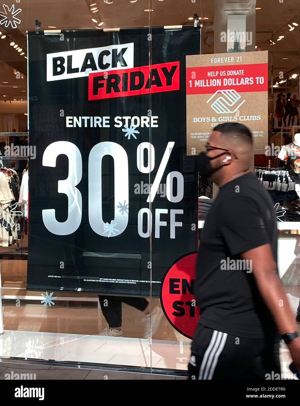 Orlando, United States. 24th Nov, 2020. A shopper wearing a face mask walks  past a Black Friday sale sign in a store window at The Mall at Millenia as  merchants prepare for