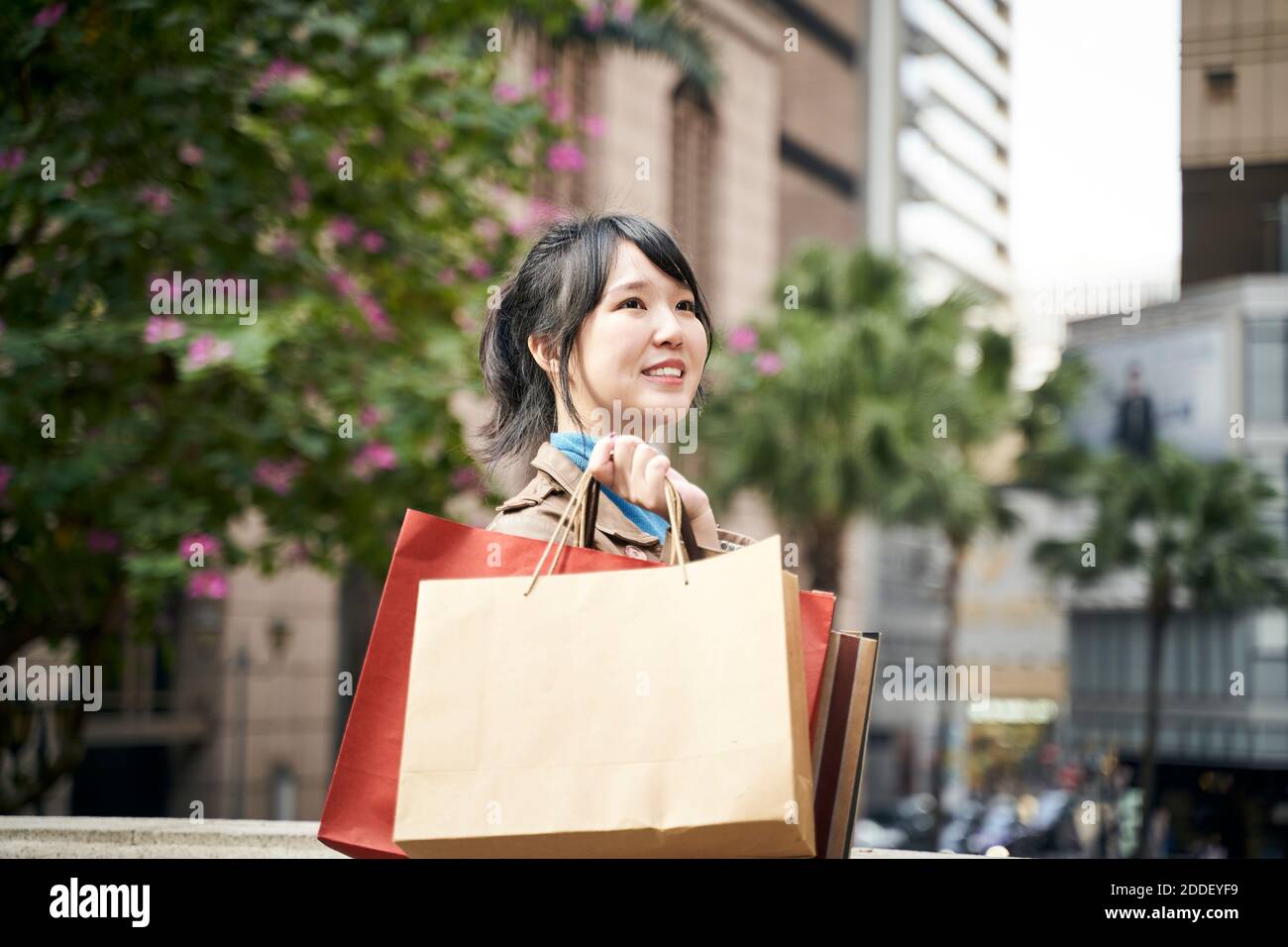 beautiful happy young asian walking on city street carrying shopping bags Stock Photo