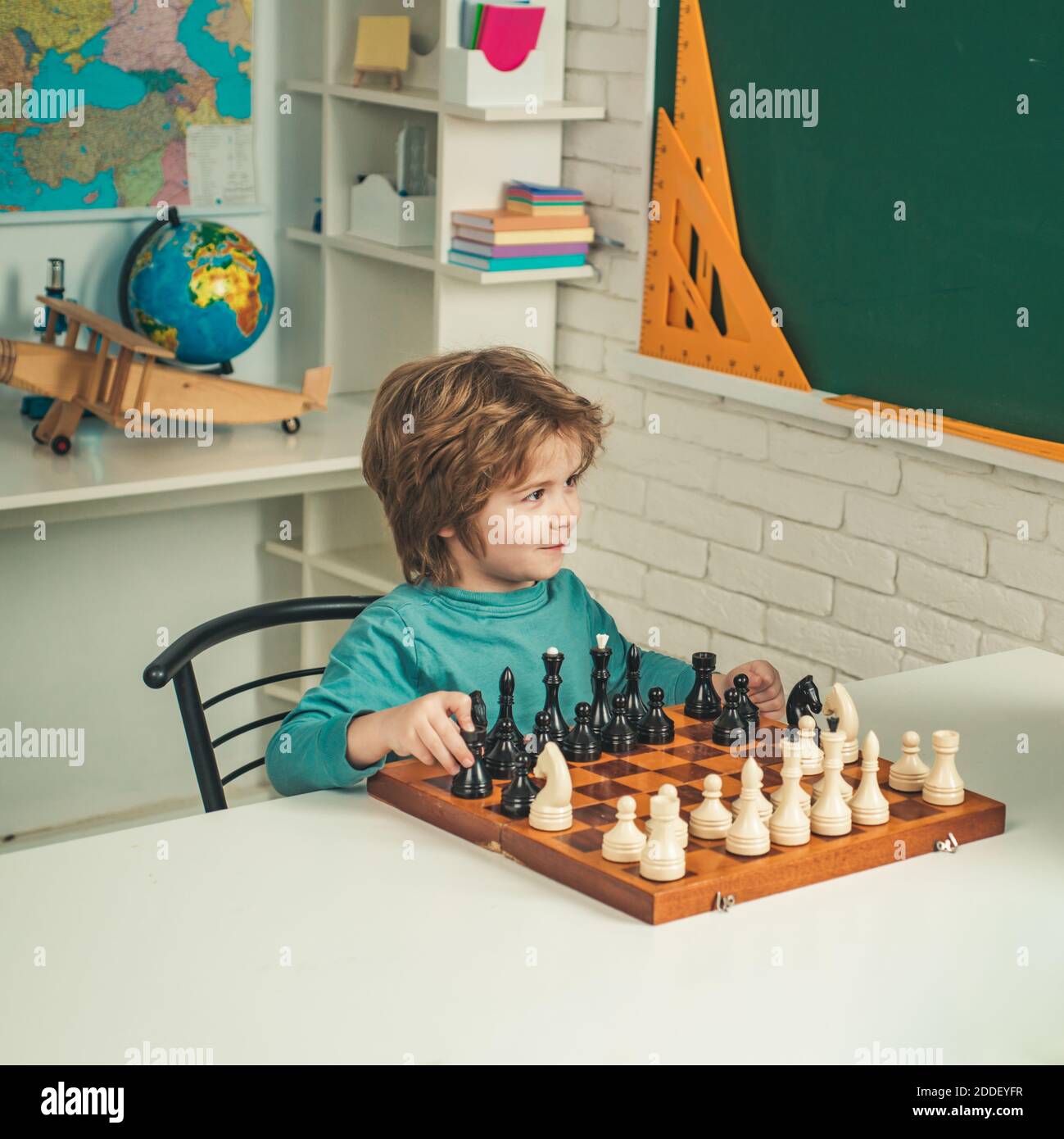 Kids educational games, early development. Kid Playing Chess. Concentrated little boy sitting at the table and playing chess. Stock Photo