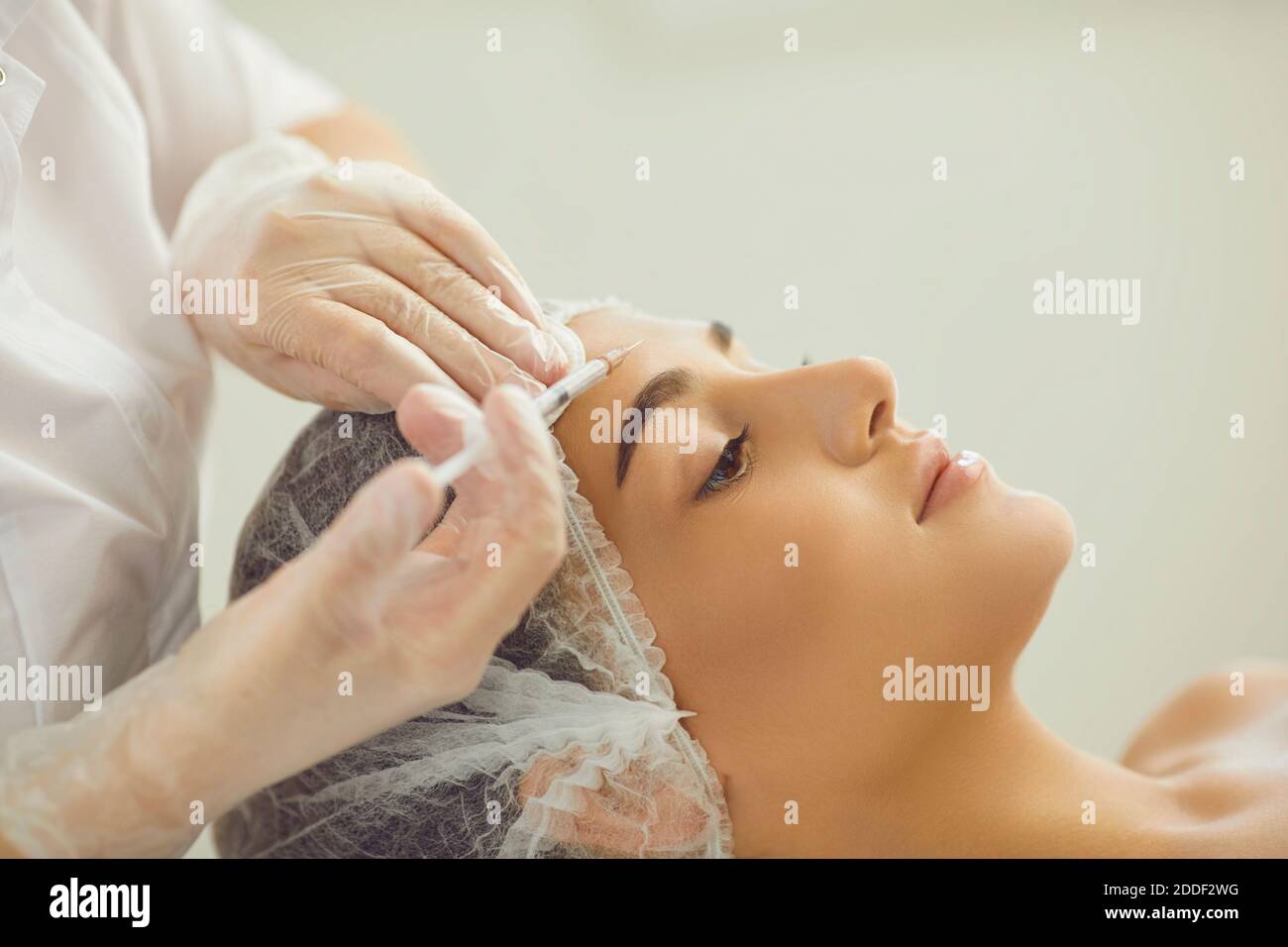 Woman recieving injection of anti-aging botox filler to forehead skin from professional cosmetologist Stock Photo