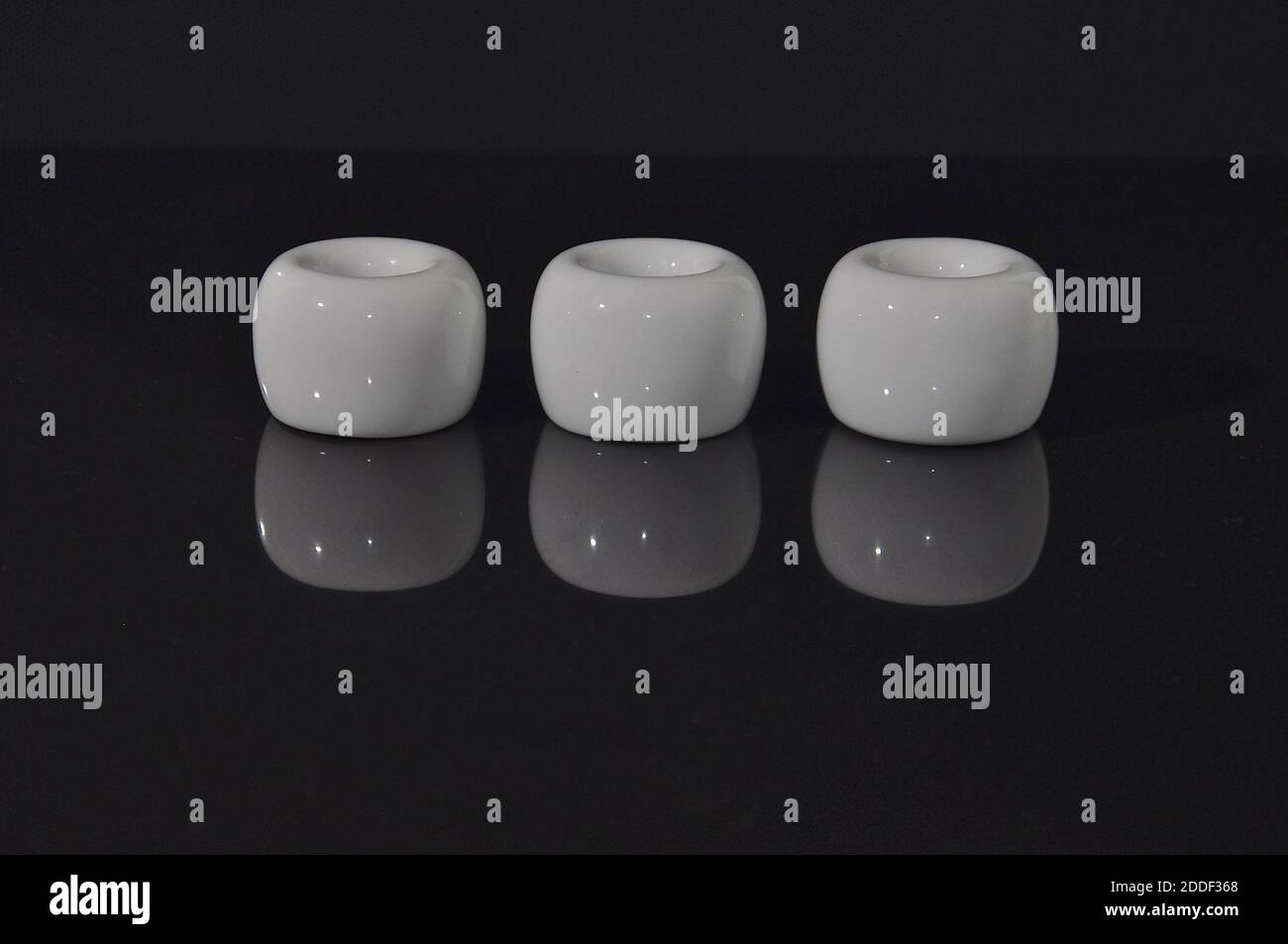A row of white ceramic cylinders on a shiny black reflective surface, showing an inverted mirror image. Stock Photo