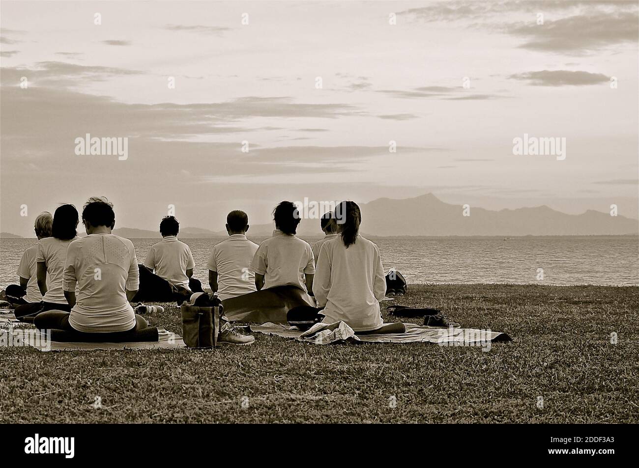 A black and white image of a group yoga session looking out on to the sea. Stock Photo