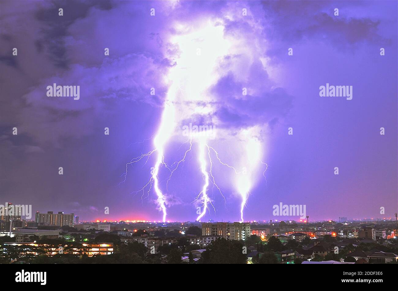 Electrical storm showing three lightening bolts hitting earth over a night time townscape. Stock Photo