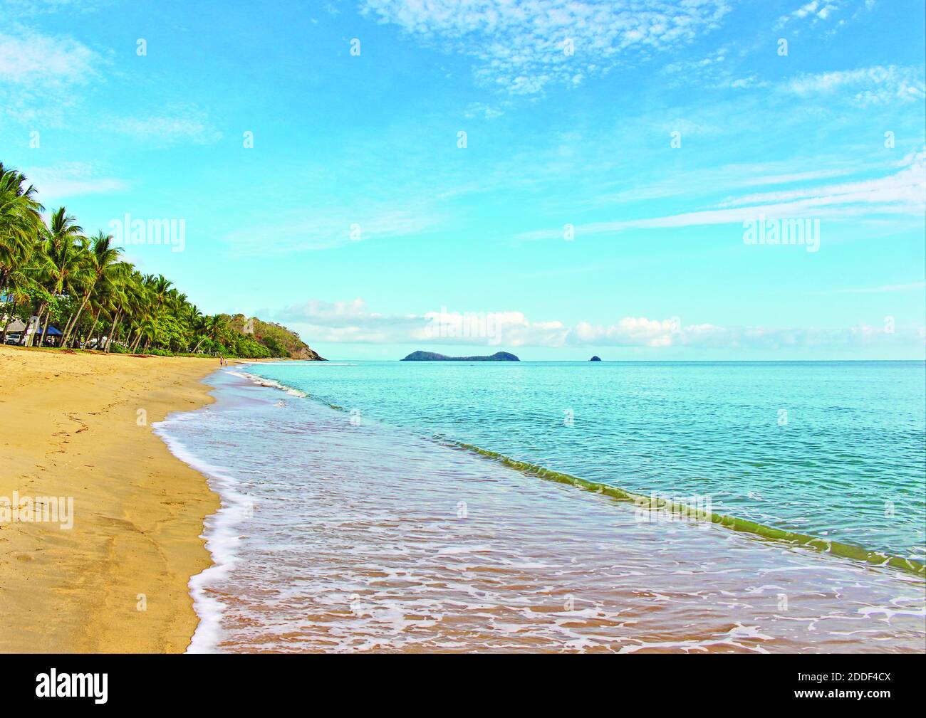 The tropical beachscape of blue sky, palm trees, lapping sea water as seen from Trinity Beach looking north towards Palm Cove and the islands offshore Stock Photo