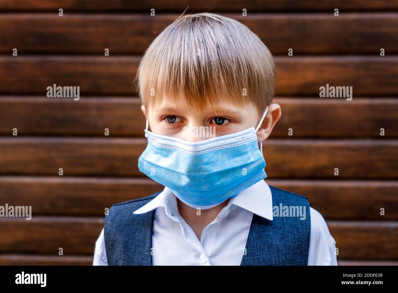 Sad Kid in a Flu Mask on the Wooden Wall Background Stock Photo
