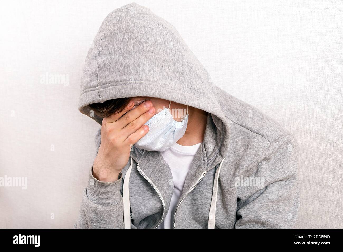 Sad Young Man in a Flu Mask by the Wall in the Room Stock Photo