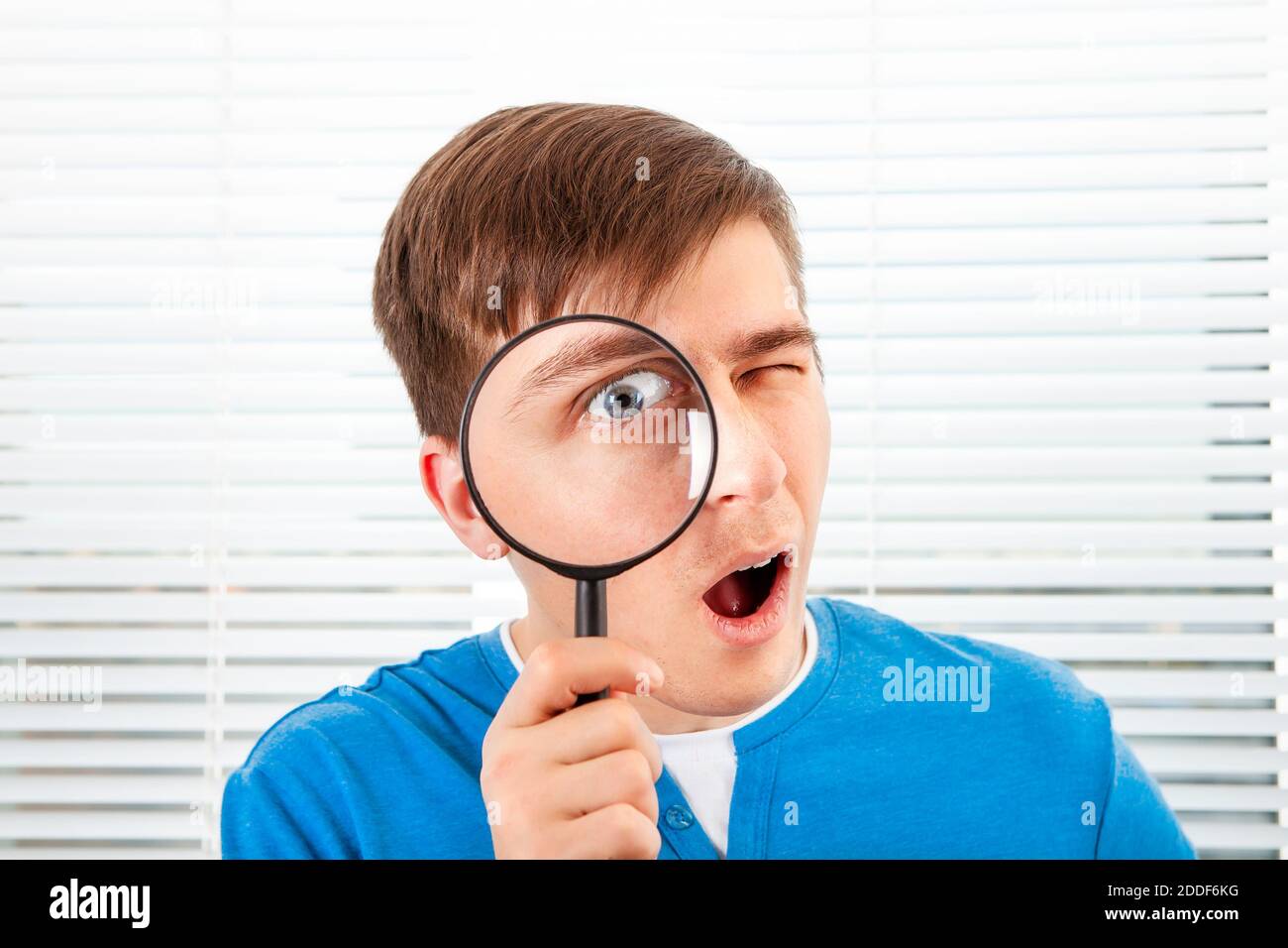 Young Man with a Magnifying Glass on the Jalousie Background closeup Stock Photo