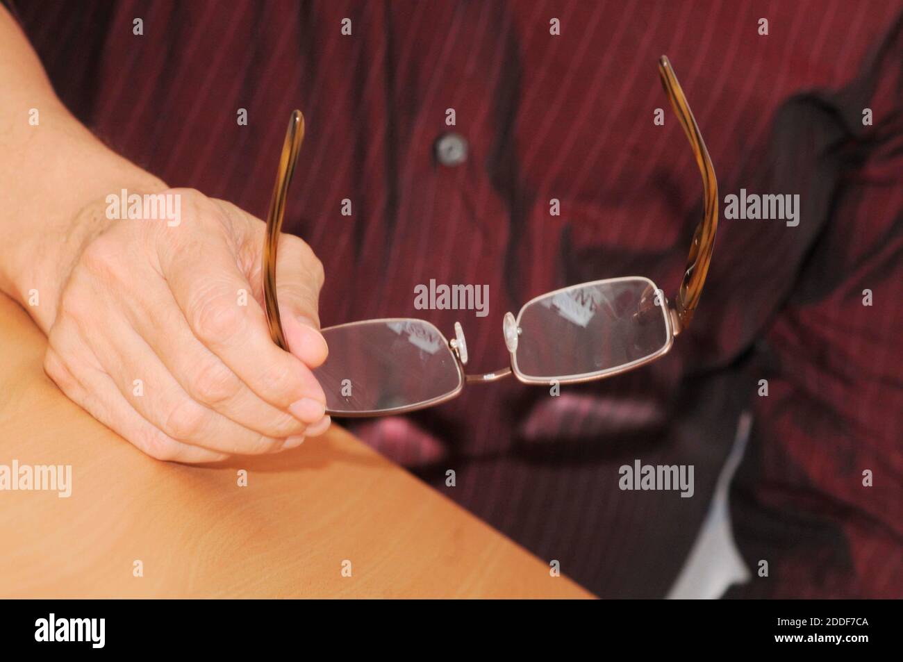 shortsighted person holding reading glasses in hand while sitting at a desk Stock Photo