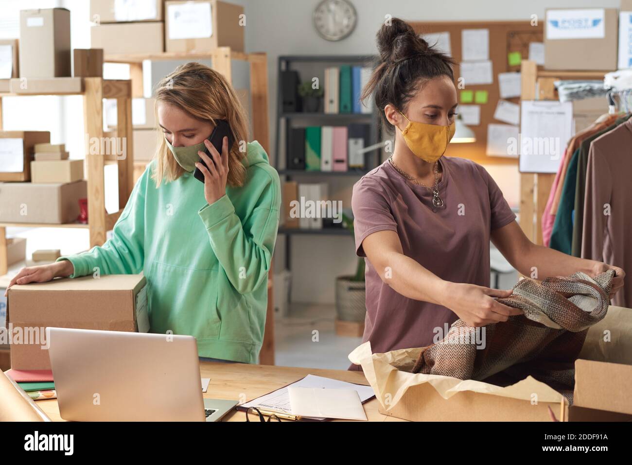 Young two women in protective masks packing clothes into the boxes working in delivery service Stock Photo
