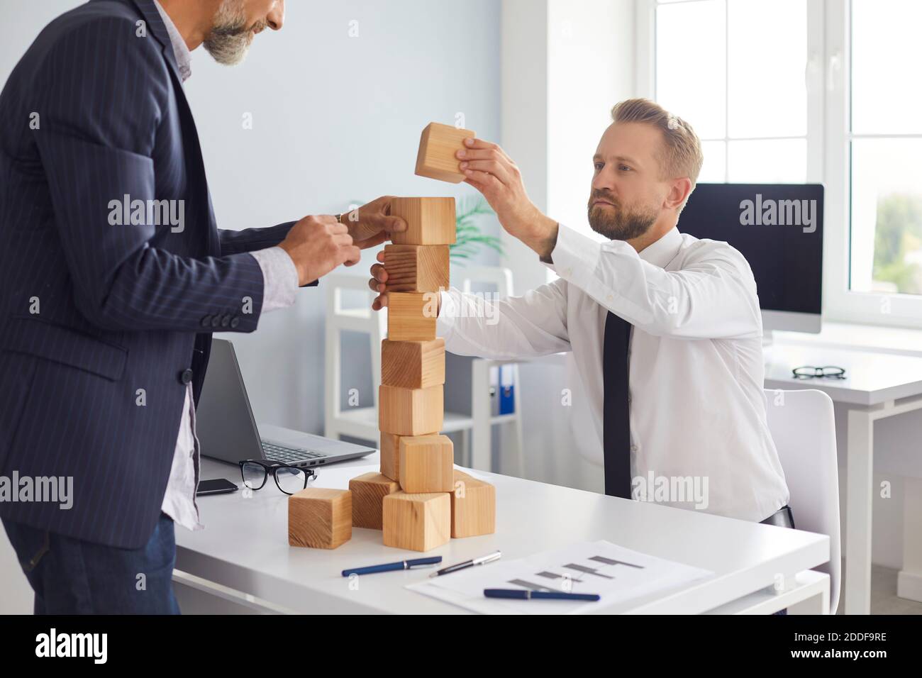 Father and son building toy block tower on office desk as metaphor of strengthening family business Stock Photo