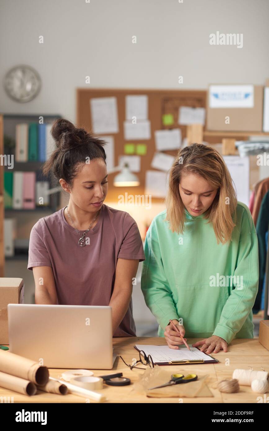Two young women working in team at the table with computer and documents standing in workshop Stock Photo
