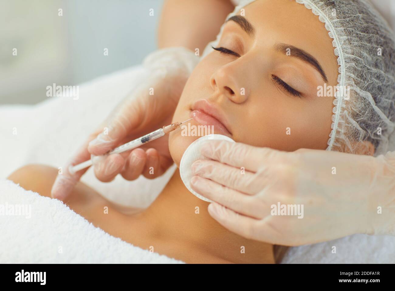 Hands of cosmetologist with syringe and cotton pad making botox filler injection in female lips Stock Photo