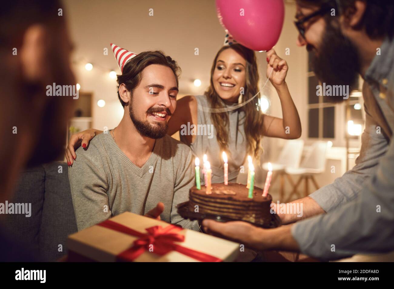 Man receives greetings and a delicious chocolate cake with burning candles given to him by friends. Stock Photo