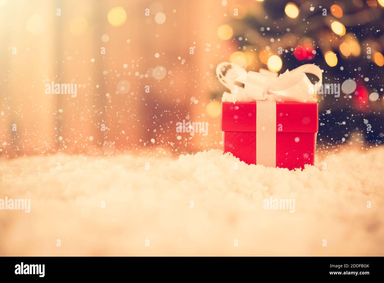 Small red gift box in the snow with blur Christmas tree in background ...