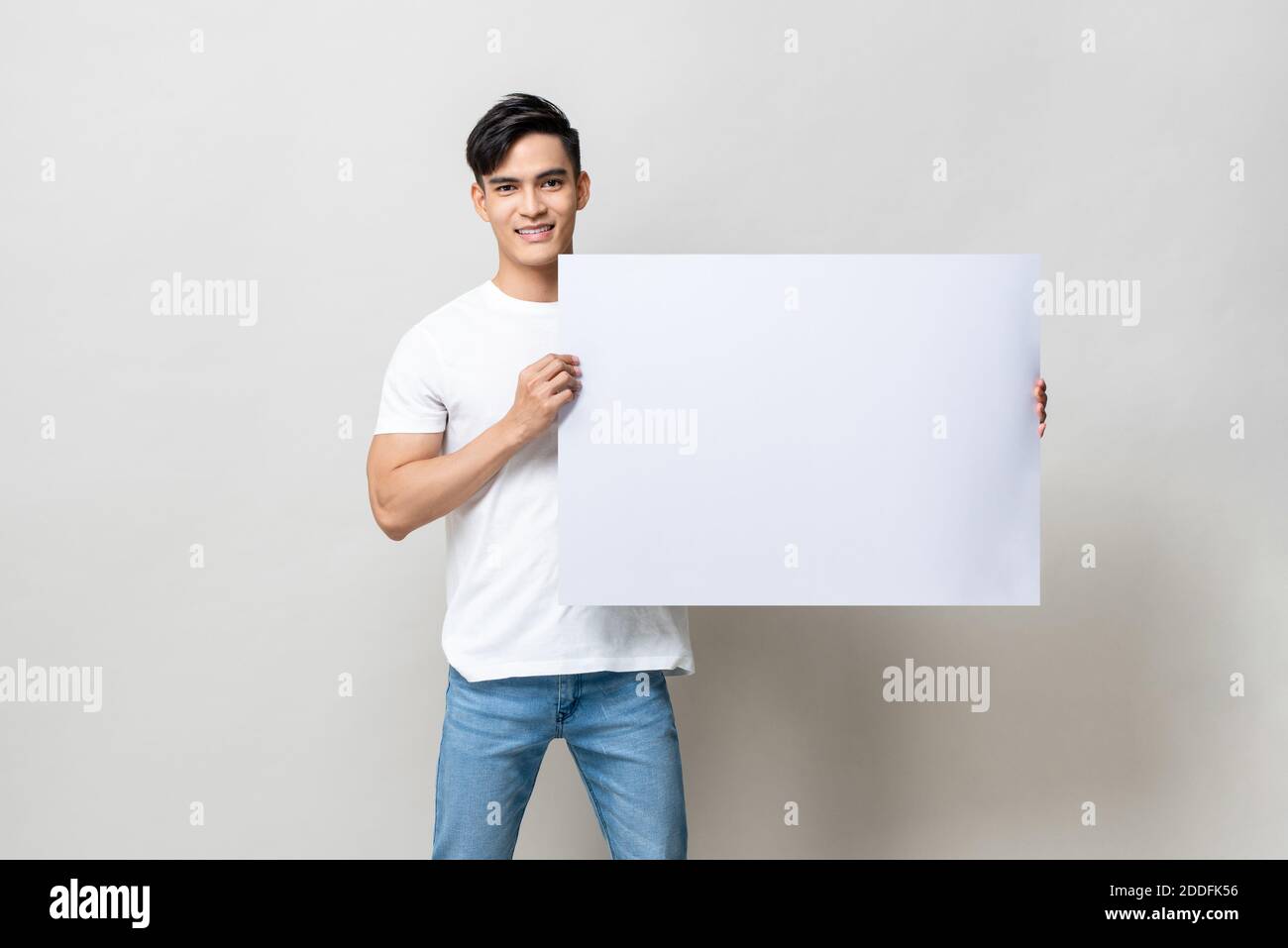Portrait of handsome Asian man holding empty white placard in isolated studio gray background Stock Photo