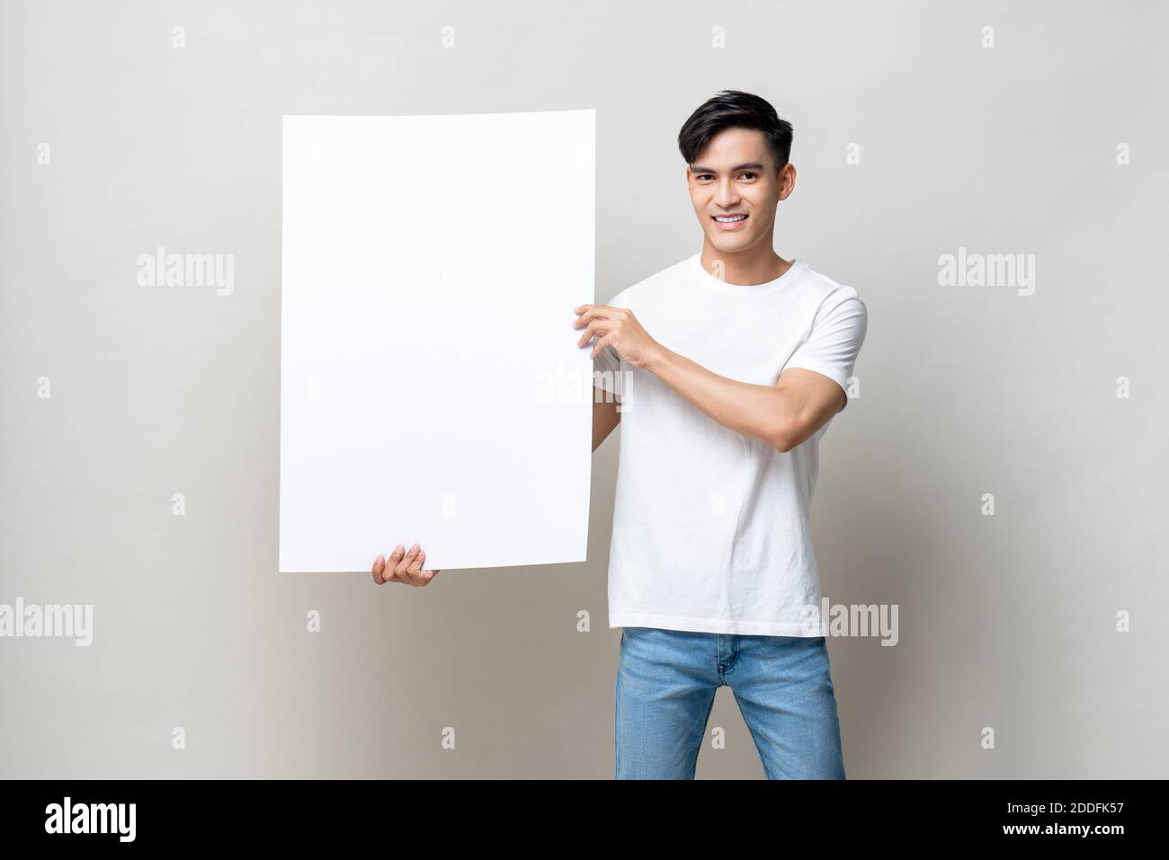 Portrait of handsome Asian man holding empty white placard in isolated studio gray background Stock Photo