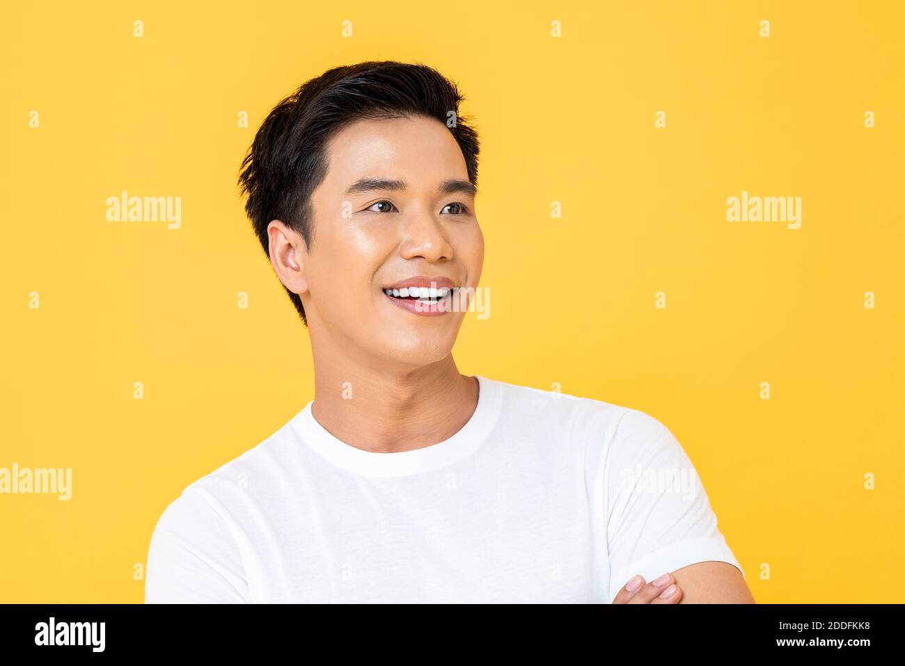 Close up portrait of young handsome Asian man cheerfully smiling and looking away in isolated studio yellow background Stock Photo