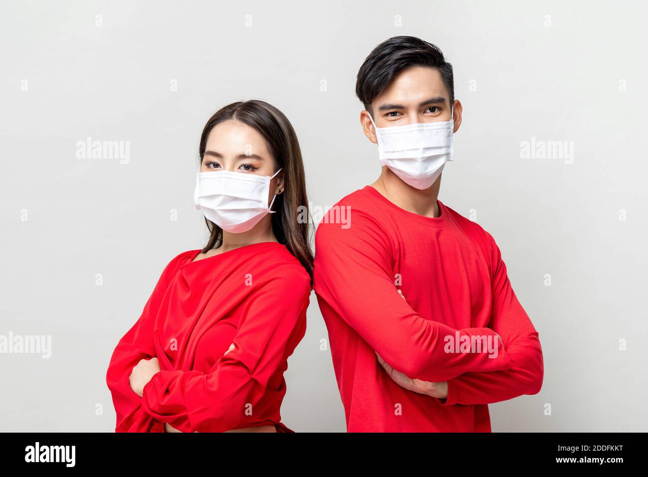 Young Asian couple wearing medical face masks and doing arms crossed gesture isolated on light gray background, Coronavirus protection concept Stock Photo