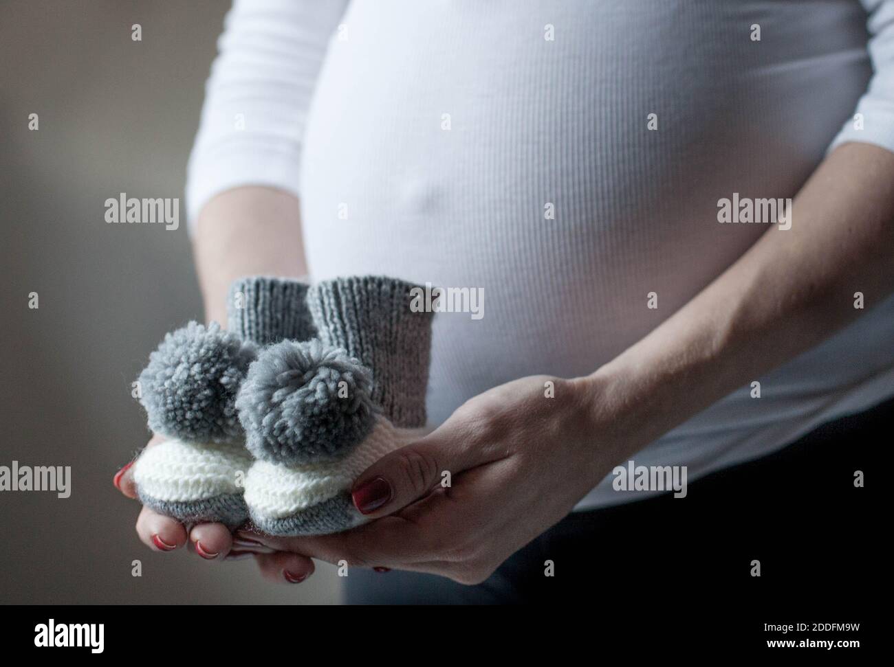 Closeup of a pregnant woman holding knitted baby socks. Coming soon concept. Expecting mother in the last trimester. Stock Photo