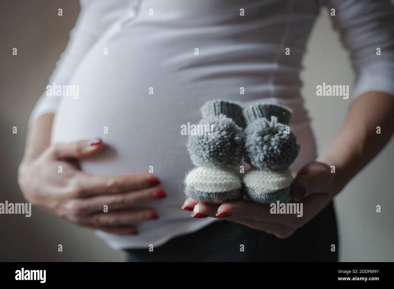 Closeup of a pregnant woman holding knitted baby socks. Coming soon concept. Expecting mother in the last trimester. Stock Photo