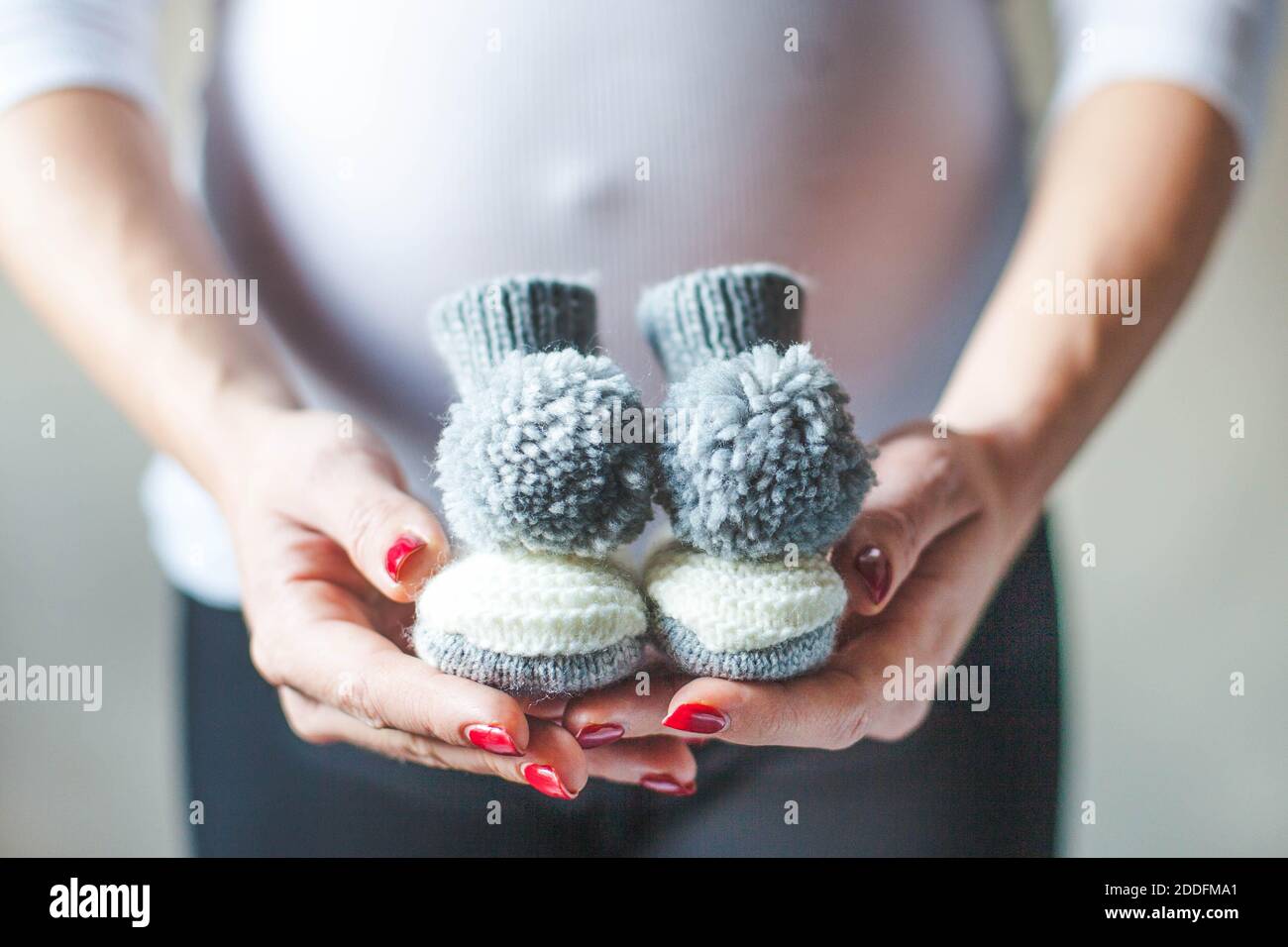 Closeup of a pregnant woman holding knitted baby socks. Coming soon concept. Expecting mother in the last trimester. Stock Photo