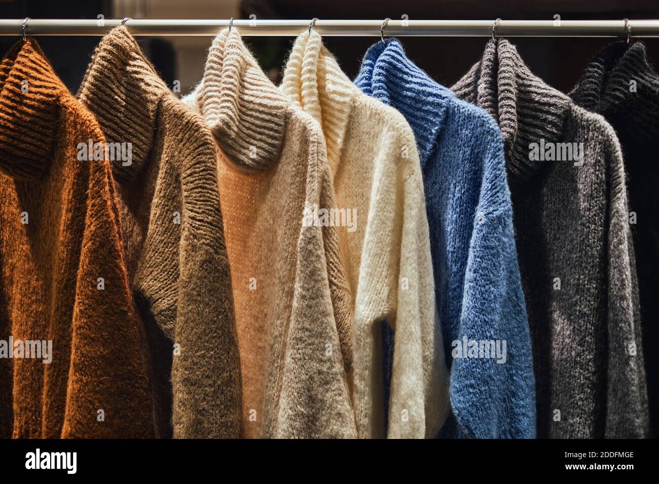 Knitted winter pullovers on a rack in a fashion store. Capsule wardrobe concept image of sweaters in cloths shop. Warm handmade wool sweaters. Stock Photo