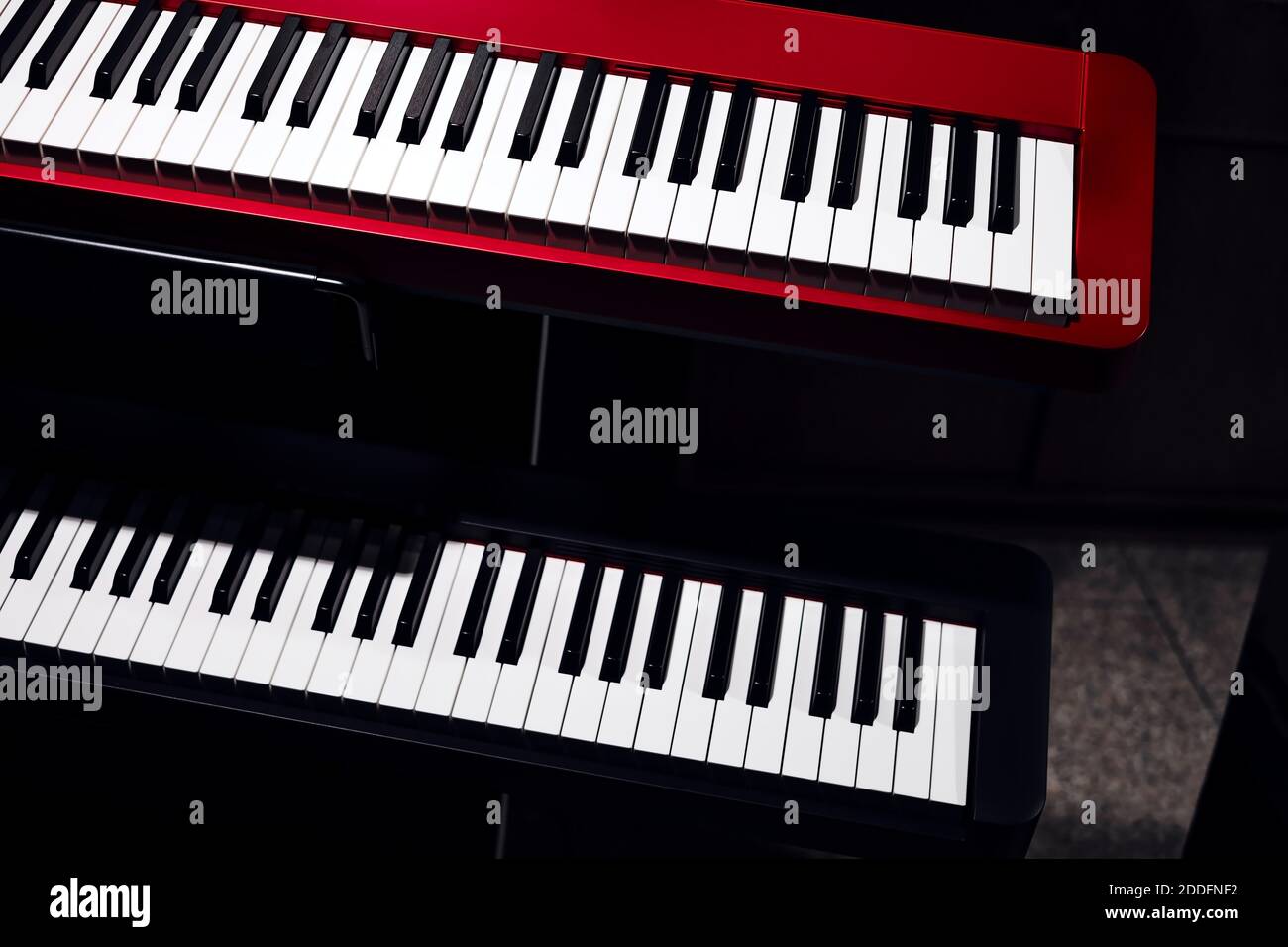 Electronic synthesizers (piano keyboards) close-up shot with dark background. Beautiful red and black musical keyboards with black and white keys. Stock Photo
