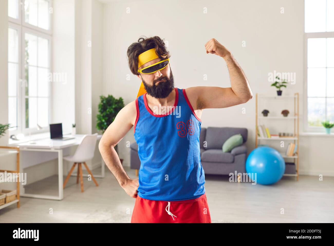 Funny sportsman boasting his thin, weak arm muscles after sport workout at home Stock Photo