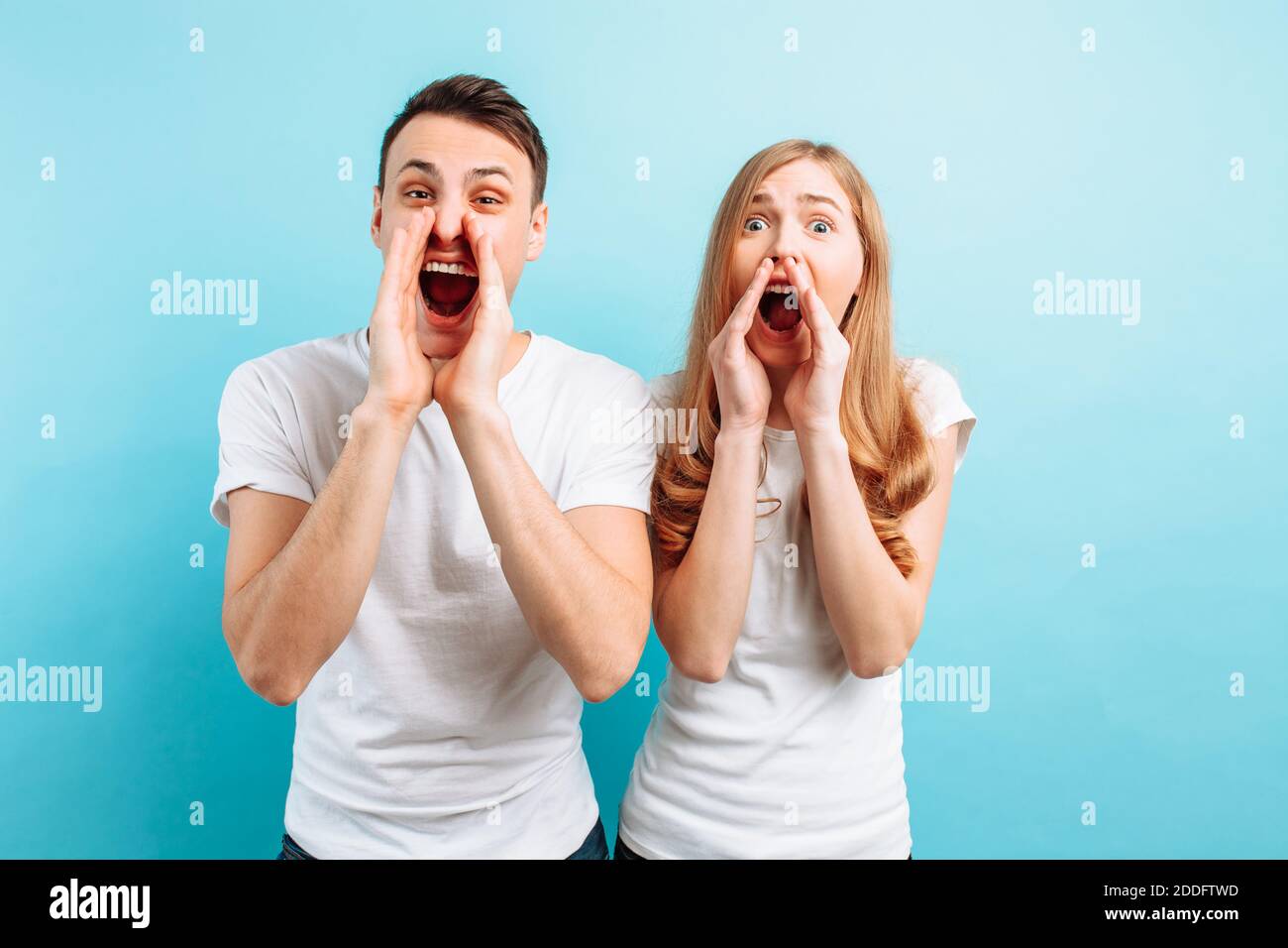 Portrait of a young couple man and woman screaming and look into the camera, against a blue background Stock Photo