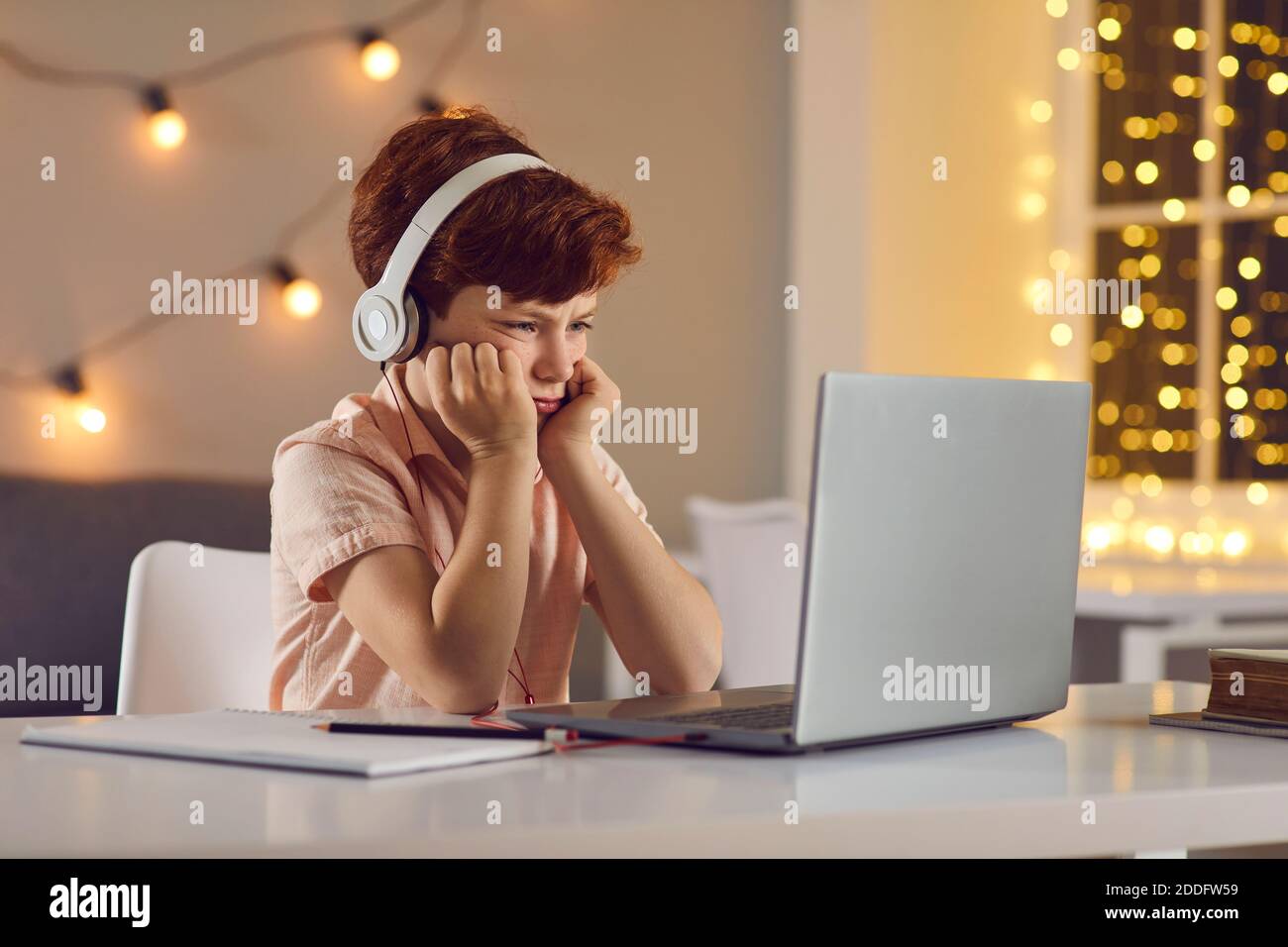 Displeased boy in headphones sitting and watching lesson or course online on laptop at home Stock Photo