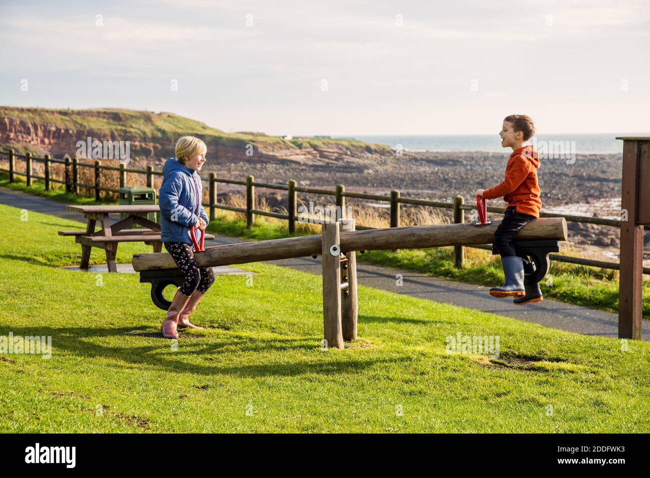 A young brother and sister playing on a seesaw in a park at Crail, Fife, Scotland. This park is on the coastal trail and is in a very beautiful locati Stock Photo