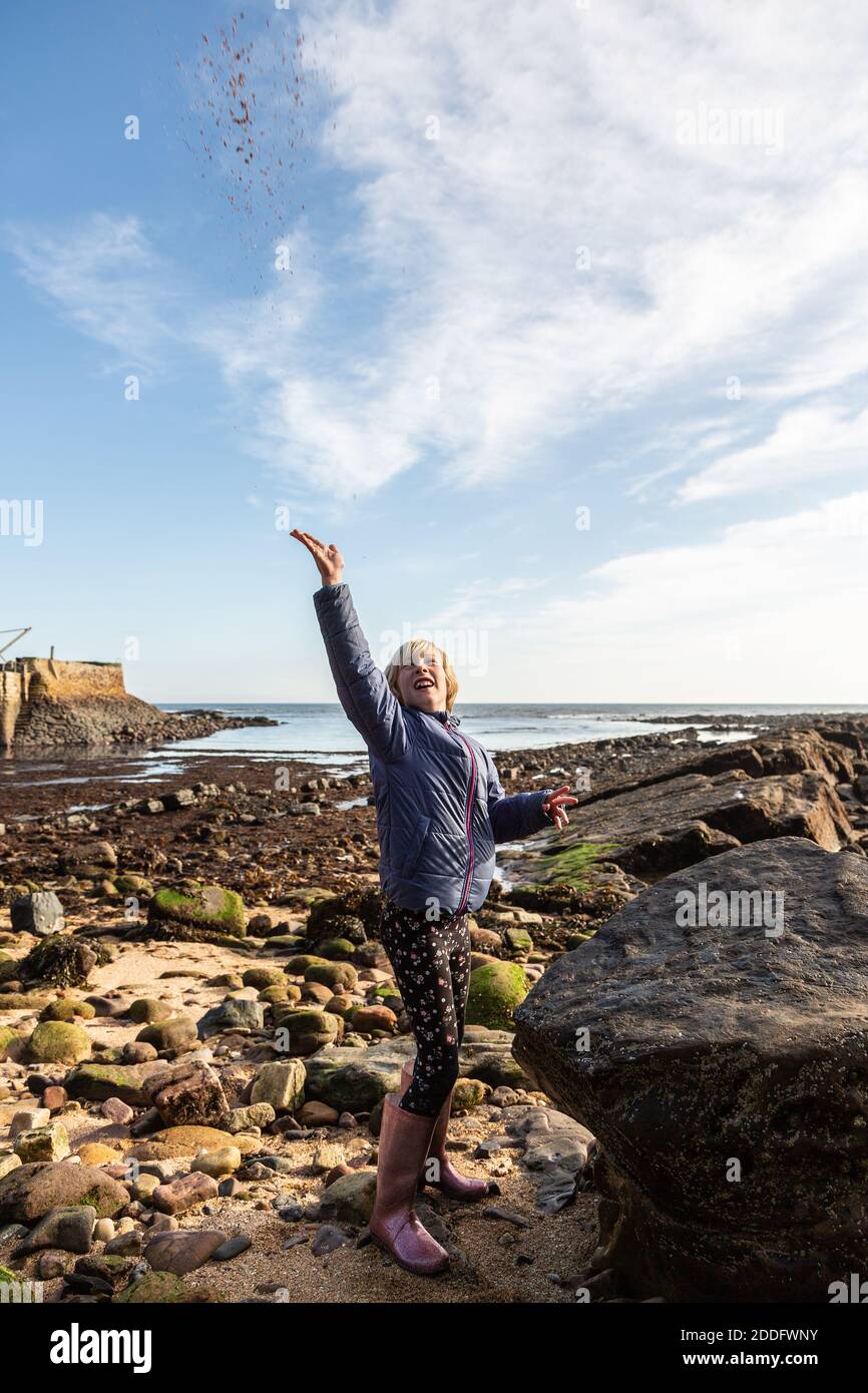 A 10 year old girl with short blond hair is throwing a handful of sand high into the air for fun at the beach in Crail, Fife, Scotland. This was on a Stock Photo
