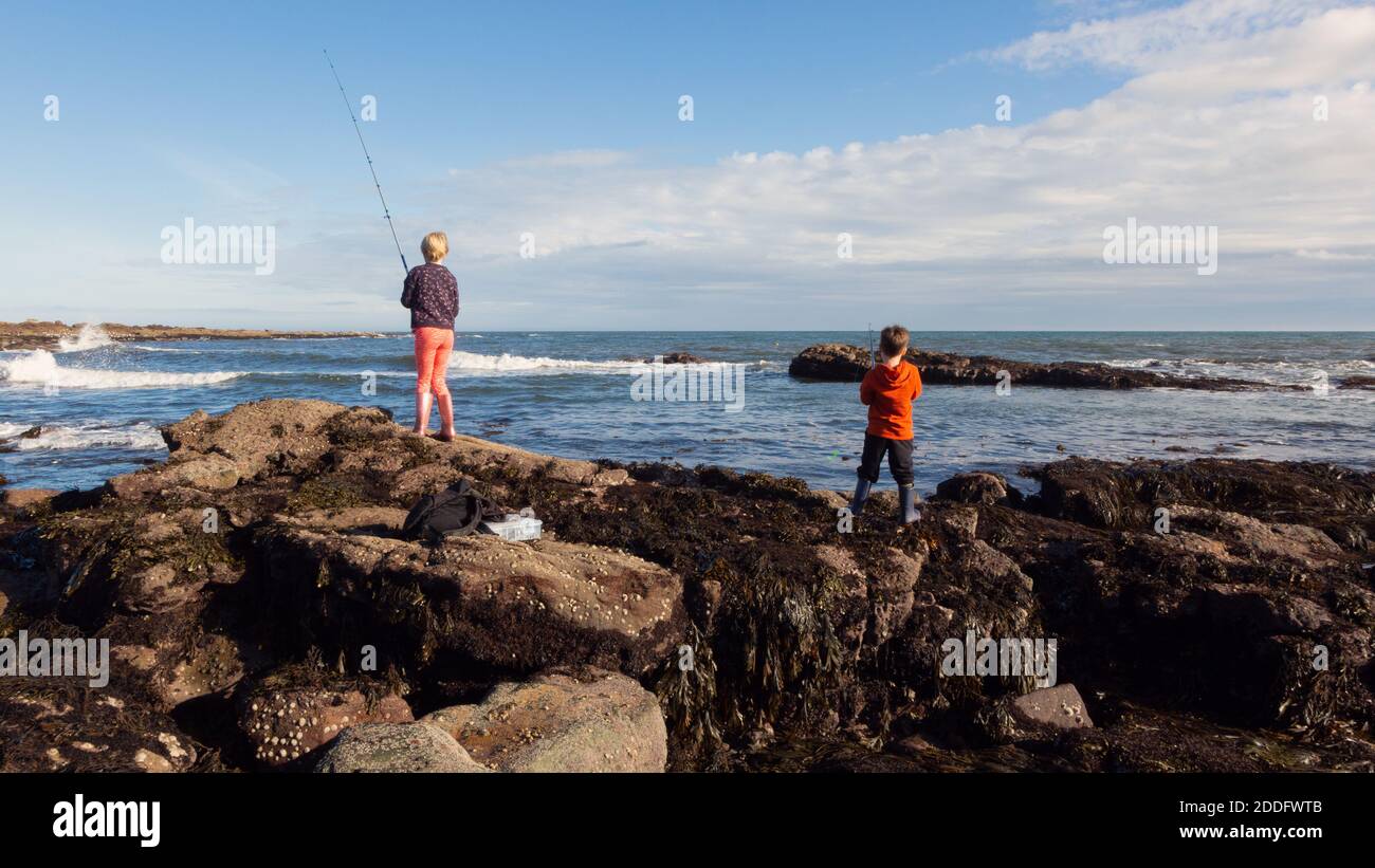 A 10yr old girl and her 6yr old brother fishing into the sea at Crail, Fife, Scotland. They love fishing (or trying to catch fish, as I call it). Stock Photo