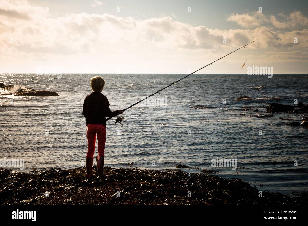 A 10yr old girl is casting a weedless lure into the sea at Crail, Fife, Scotland. There was lots of seaweed in the area and the weedless lure prevents Stock Photo