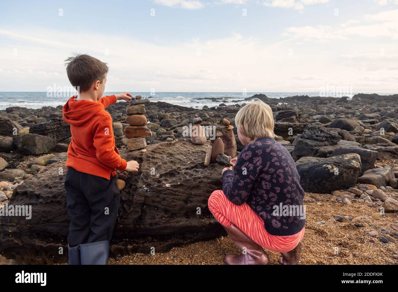 Siblings putting the finishing touches to their little rock people creations. This is a great way to spend time on a beach holiday. Stock Photo
