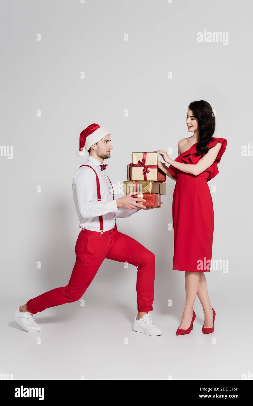 Man in santa hat holding gifts near smiling woman in red dress and ...
