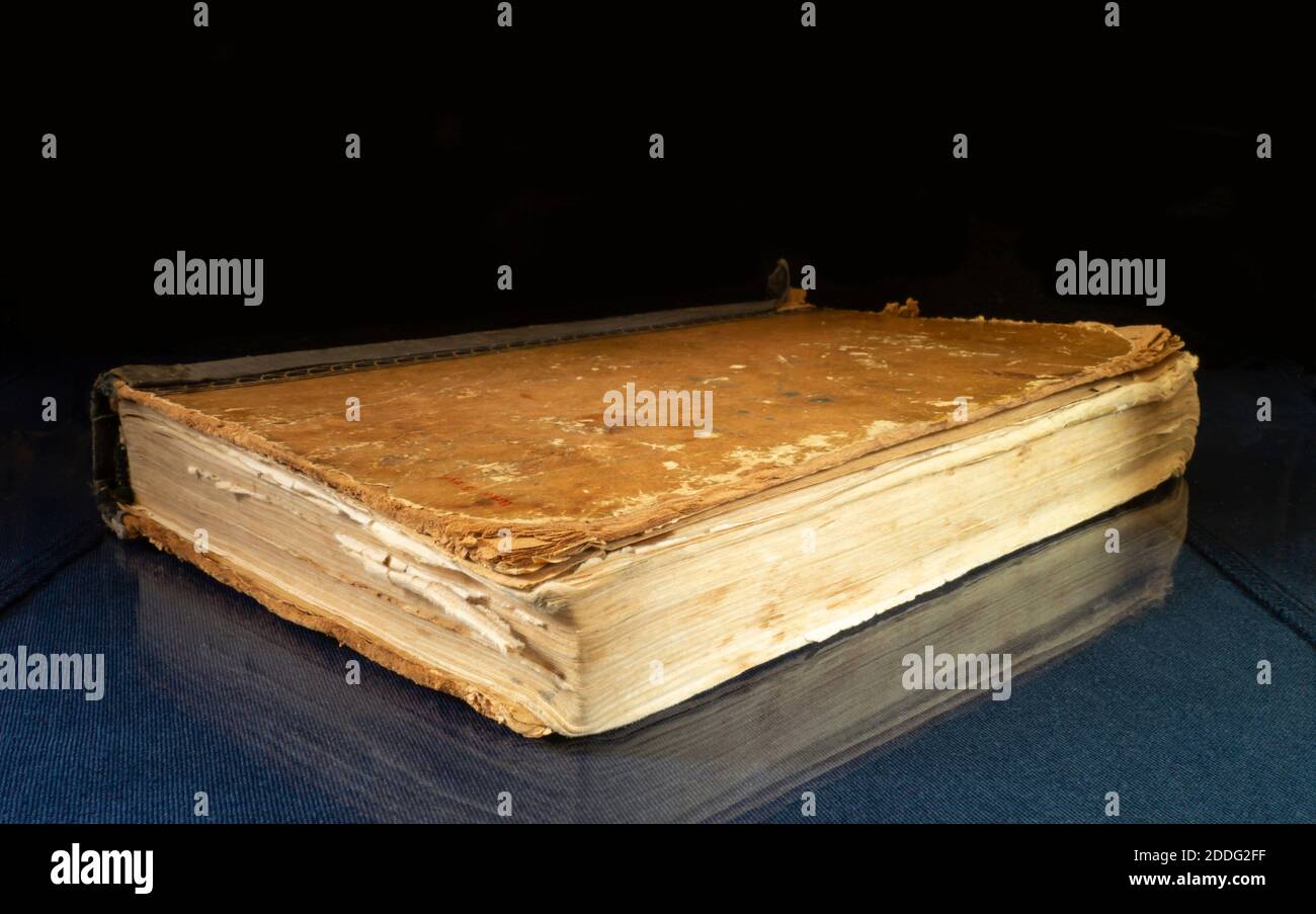 Aging book rests upon glass table with reflection. Subjects on black background close-up Stock Photo