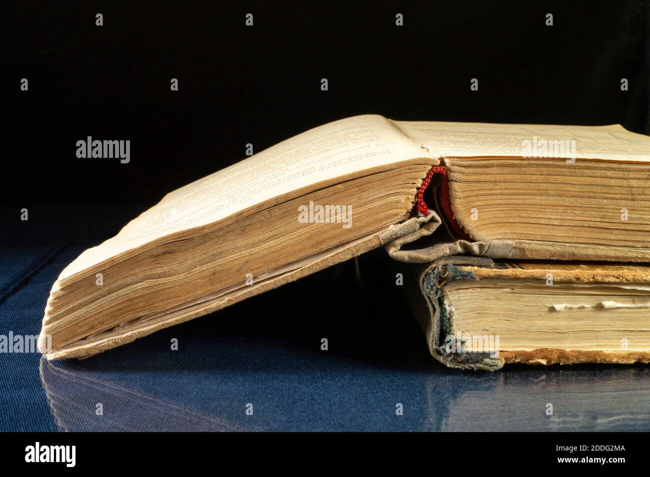 Aging book rests upon glass table with reflection. Subjects on black background close-up Stock Photo