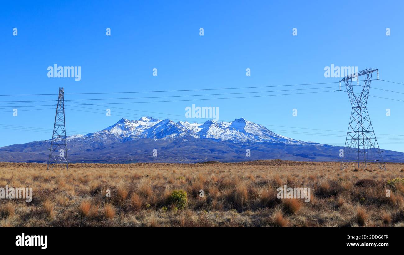 Mount Ruapehu, New Zealand, seen from the tussock lands of the Rangipo Desert, with power pylons in the foreground Stock Photo